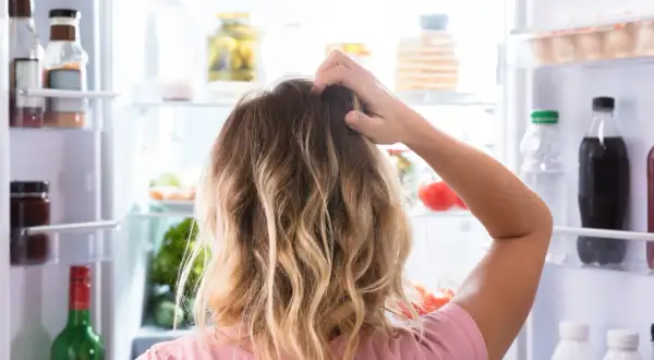 Kvinna kliar sig i huvudet framför ett kylskåp fyllt med mat. Svårt att välja vad som passar en diet på 1500 kalorier per dag.