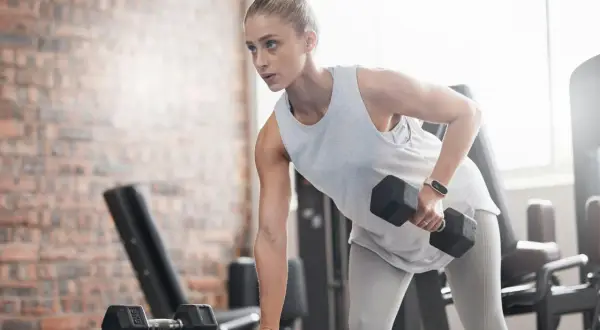 En kvinna med ektomorf kroppstyp tränar rygg med hantlar på ett gym.