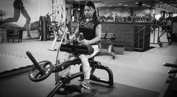 Kvinna tränar vaderna på en sittande vadpress-maskin i ett modernt gym.