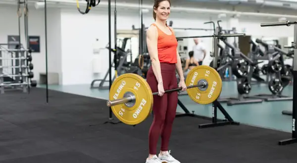 Kvinna i gym utför marklyft med skivstång. Ett effektivt marklyft program kan stärka hela kroppen.