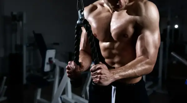 Muskulös man utför triceps pushdown med rep i ett gym.