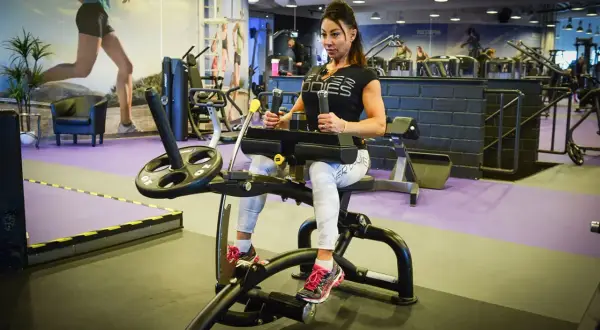 Kvinna tränar magen på gymmaskin. Hon har på sig träningskläder och fokuserar på sin vad press.