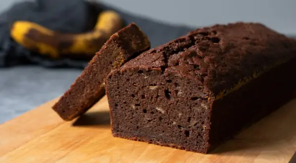 En saftig banankaka utan socker, med en skiva uppskuren. Bakom syns en mogen banan.