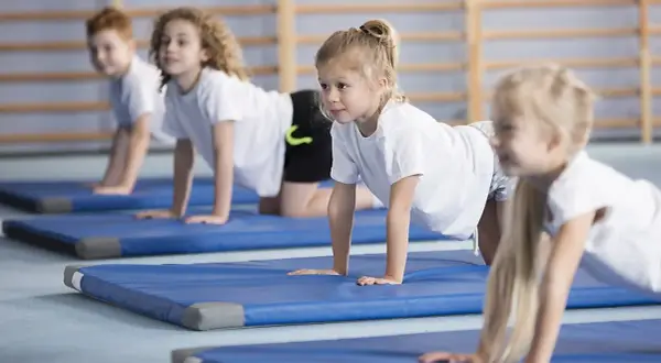 Barn på gympaövning, en aktivitet som motverkar stillasittande barn. De ligger på blåa mattor i en gymnastikhall.
