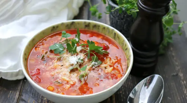 En mustig tomatsoppa med ris och örter, en perfekt källa till vegetariskt protein. Serveras med en sked och pepparkvarn.