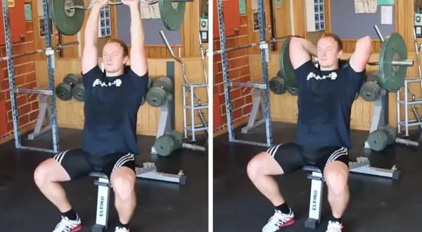 Man utför french press i gym. Han sitter på en bänk och lyfter en skivstång över huvudet.