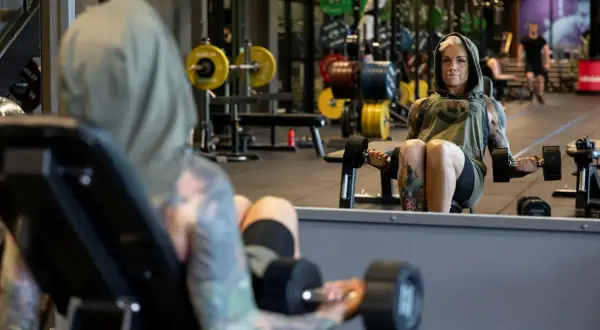 En kvinna med tatuerad crossfit kropp lyfter vikter på gymmet.