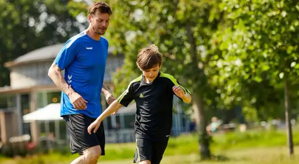 En man och en pojke springer på en gräsmatta, kanske på väg till ett **barn gym** eller en fotbollsträning.