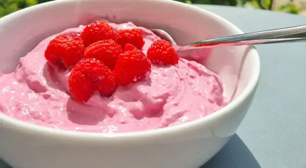 En skål med rosa krämig dessert toppad med färska hallon, perfekt för ett nyttigt fika på jobbet.