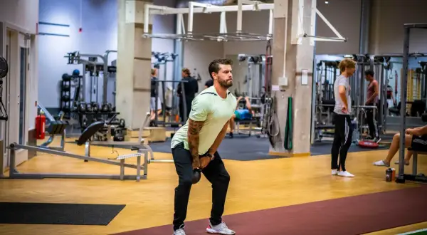 Man utför ett helkroppspass på gym med kettlebell.