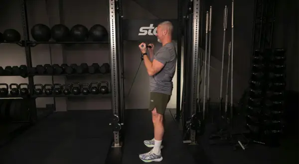 Man utför bicepscurl med stång i ett gym. I bakgrunden syns vikter och träningsutrustning.