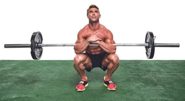 Muskulös man utför en zercher squat med skivstång i armvecken.