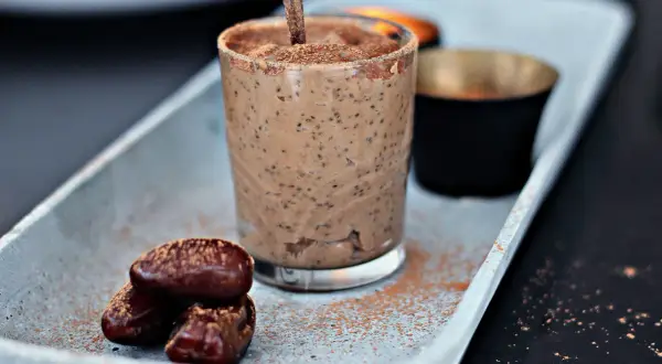 A glass of creamy chia pudding with dates and cocoa powder on a tray.