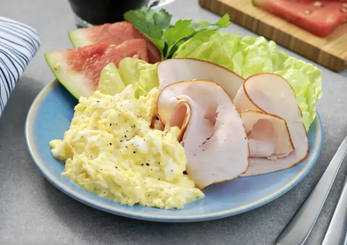 En blå tallrik med äggröra, kalkonpålägg, sallad och vattenmelon. Ett perfekt 5:2 recept för en lätt lunch.