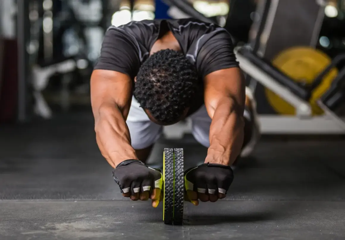Man gör en ab wheel rollout i gymmet, med fokus på magmusklerna.