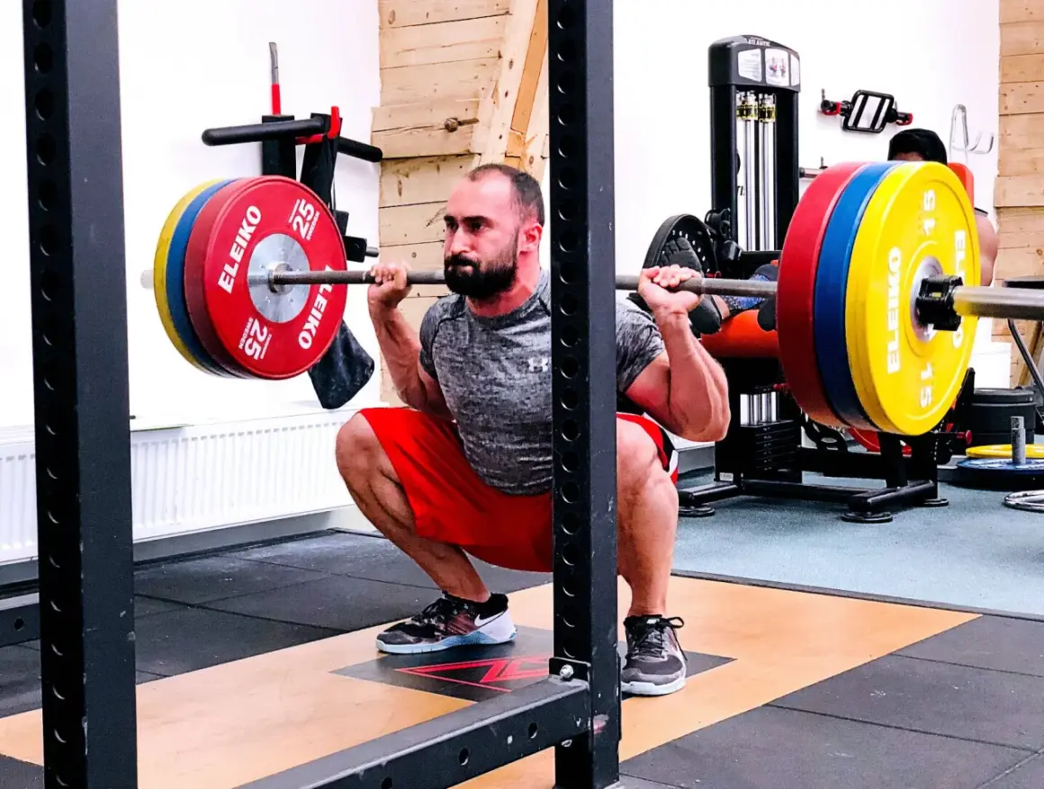 Man utför en djup knäböj med skivstång, en klassisk övning som en del av sin russian squat routine.