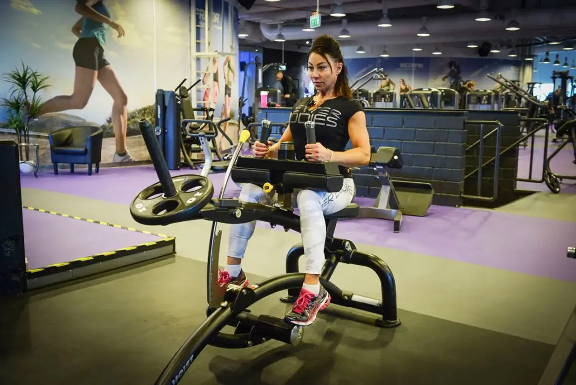 Kvinna tränar magen på gymmaskin. Hon har på sig träningskläder och fokuserar på sin vad press.