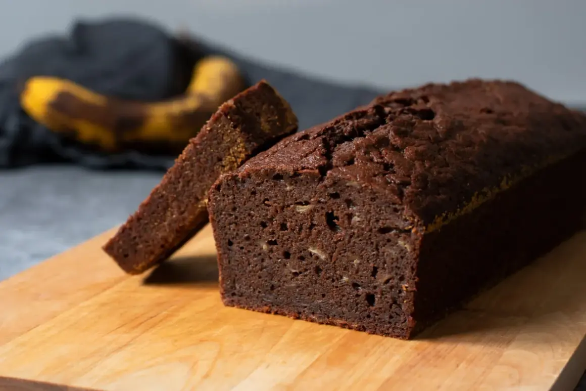 En saftig banankaka utan socker, med en skiva uppskuren. Bakom syns en mogen banan.