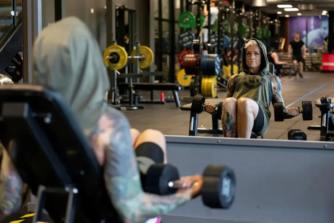 En kvinna med tatuerad crossfit kropp lyfter vikter på gymmet.