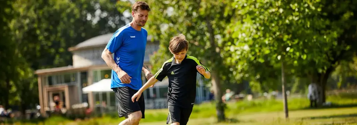 En man och en pojke springer på en gräsmatta, kanske på väg till ett **barn gym** eller en fotbollsträning.
