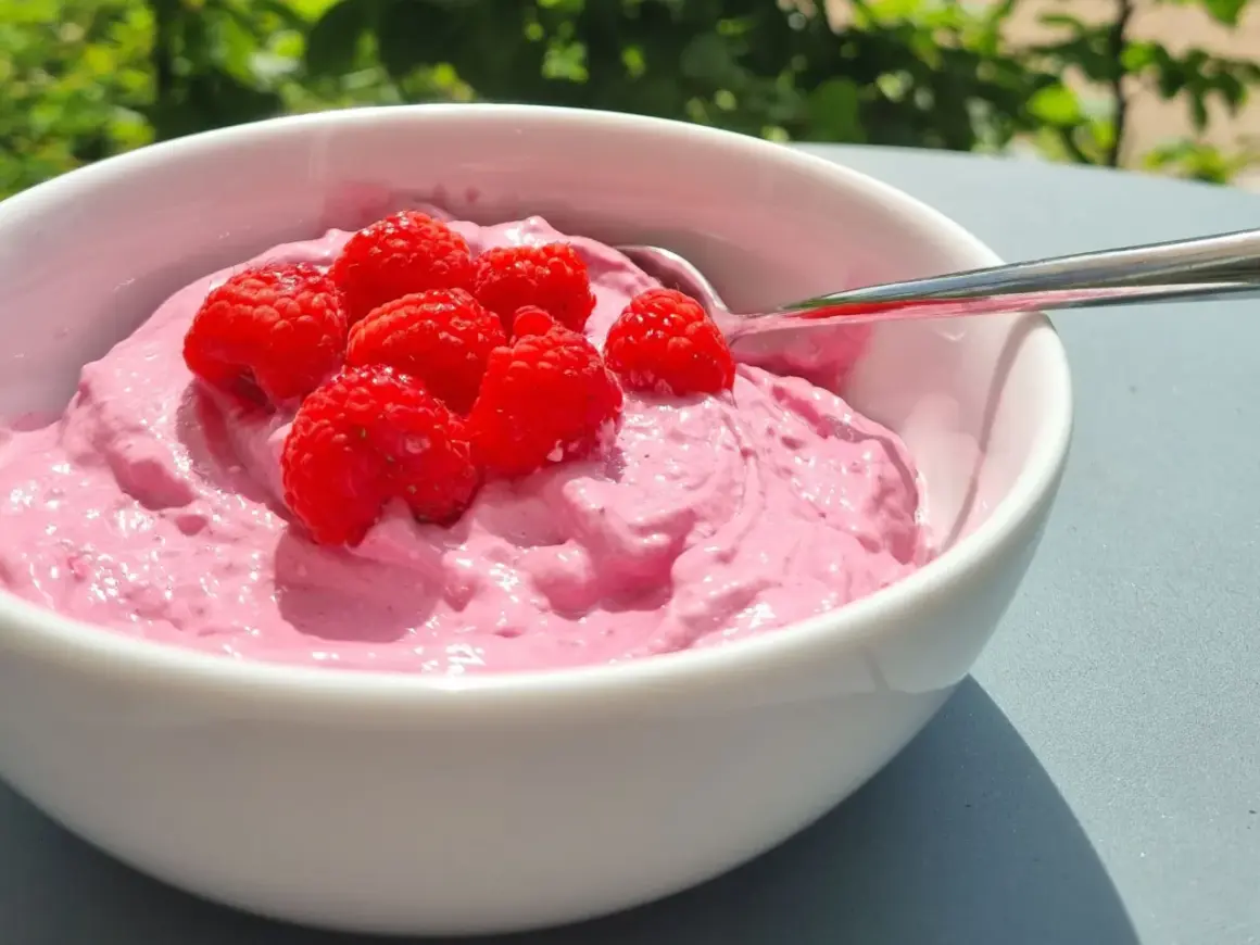 En skål med rosa krämig dessert toppad med färska hallon, perfekt för ett nyttigt fika på jobbet.