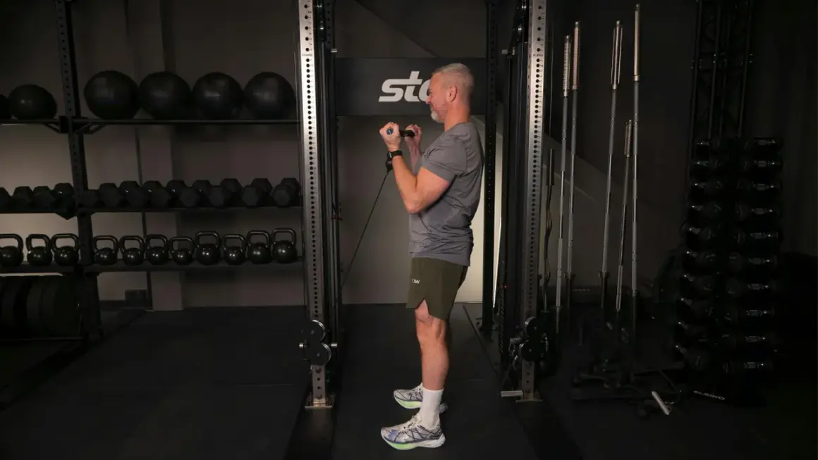Man utför bicepscurl med stång i ett gym. I bakgrunden syns vikter och träningsutrustning.