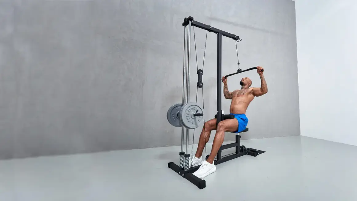 Man tränar latsdrag muskler på ett gym. Han sitter på en bänk och drar ner en stång med vikter.