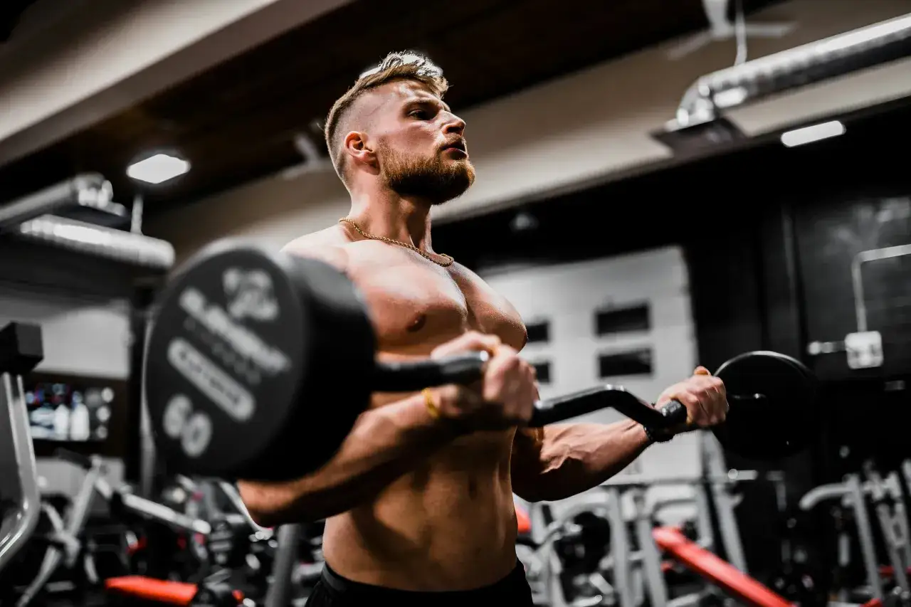 En muskul&ouml;s man lyfter en skivst&aring;ng i ett gym. Han fokuserar p&aring; tr&auml;ningen, en viktig del av hur blir man stark.