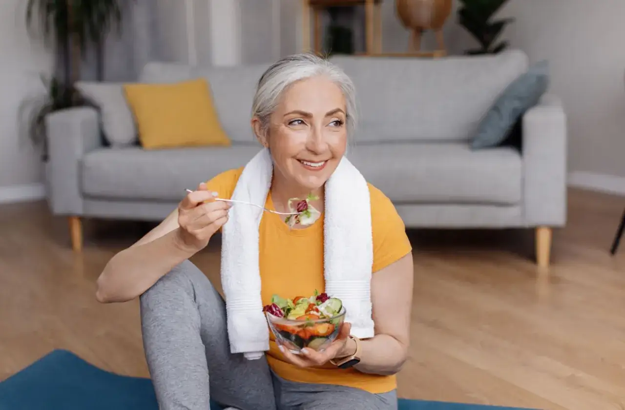 Glad kvinna äter sallad efter träning, en del av att bygga muskler efter 50.