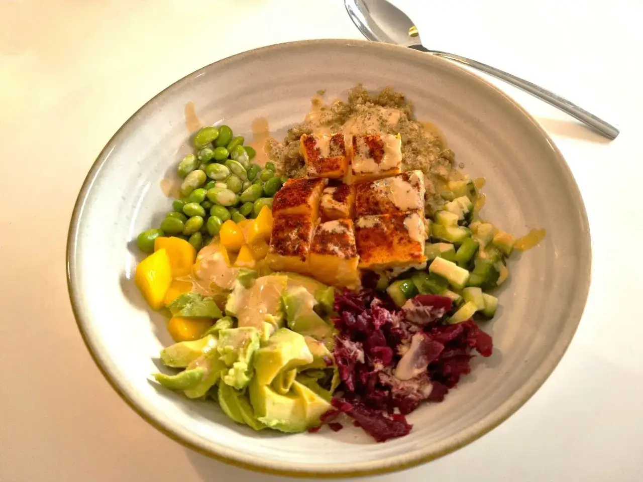 En sk&aring;l med nyttig mat: lax, quinoa, edamame, mango, avokado, gurka och r&ouml;dbetor. Ett perfekt recept f&ouml;r en h&auml;lsosam m&aring;ltid.