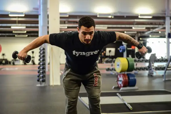 Man tränar baksida axlar med hantlar på gym.