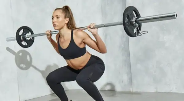En kvinna med en imponerande fitness kropp utför ett knäböj med skivstång.