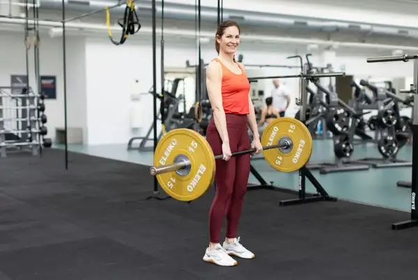 Kvinna i gym utför marklyft med skivstång. Ett effektivt marklyft program kan stärka hela kroppen.