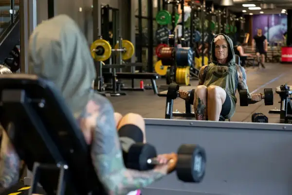 En kvinna med tatuerad crossfit kropp lyfter vikter på gymmet.